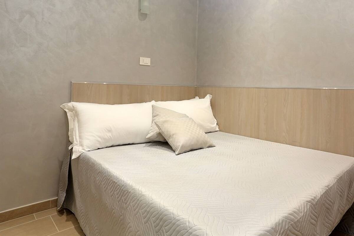 A neatly made bed with a wooden headboard and a textured white bedspread.