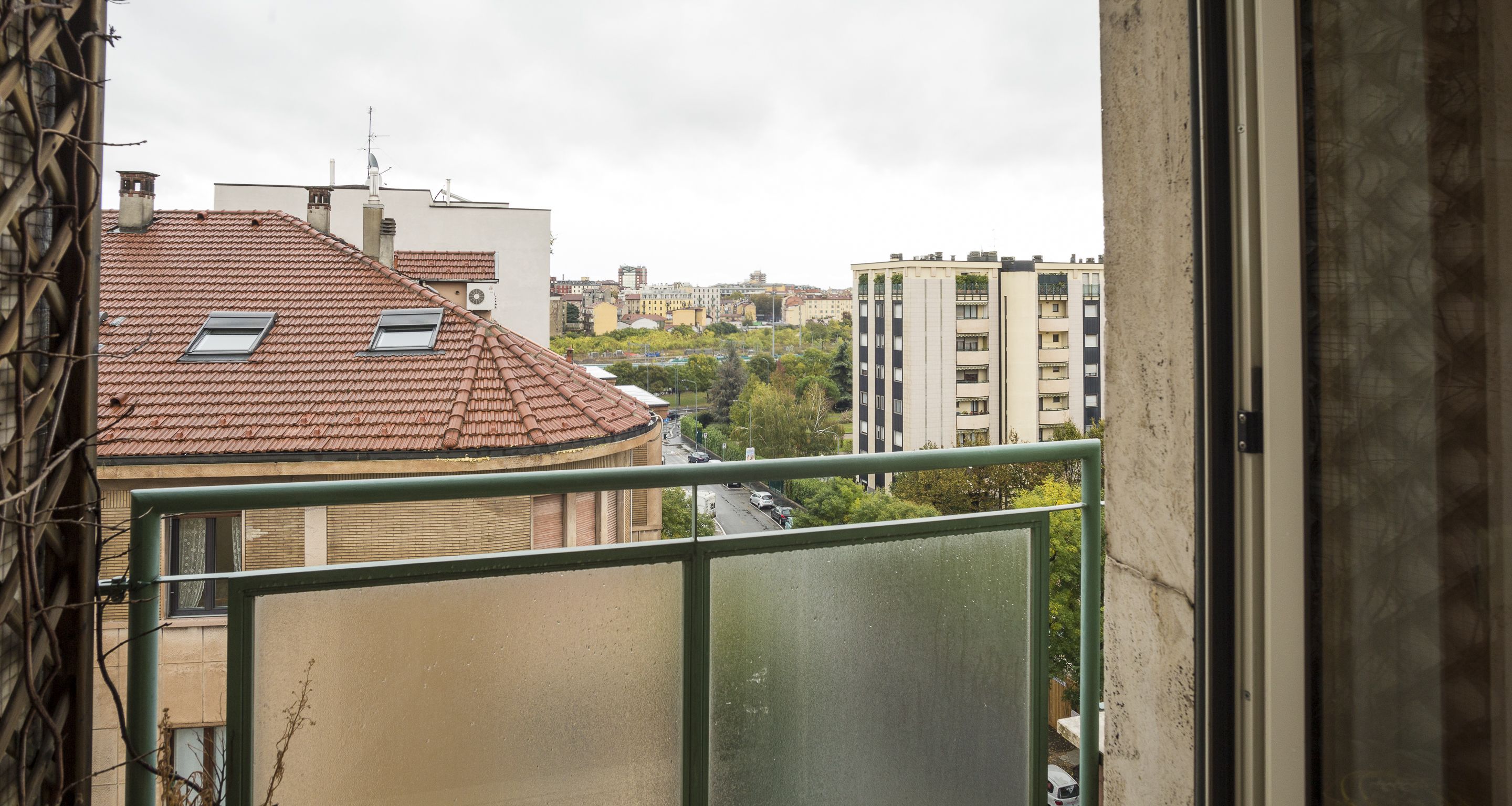 A view from a balcony overlooking a cityscape with buildings, a road, and greenery.