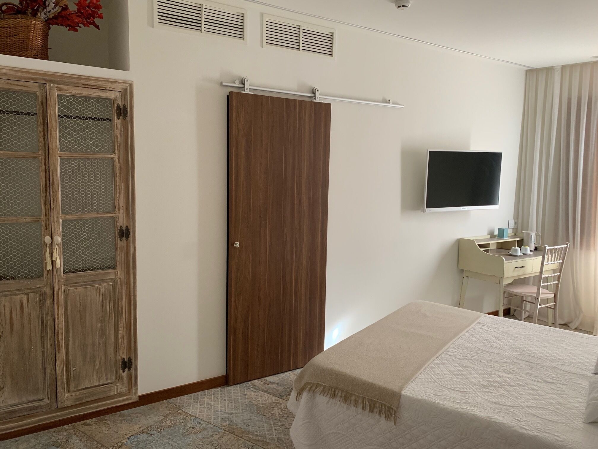 Un dormitorio con cama, armario, escritorio con silla, televisor y ventana con cortinas.