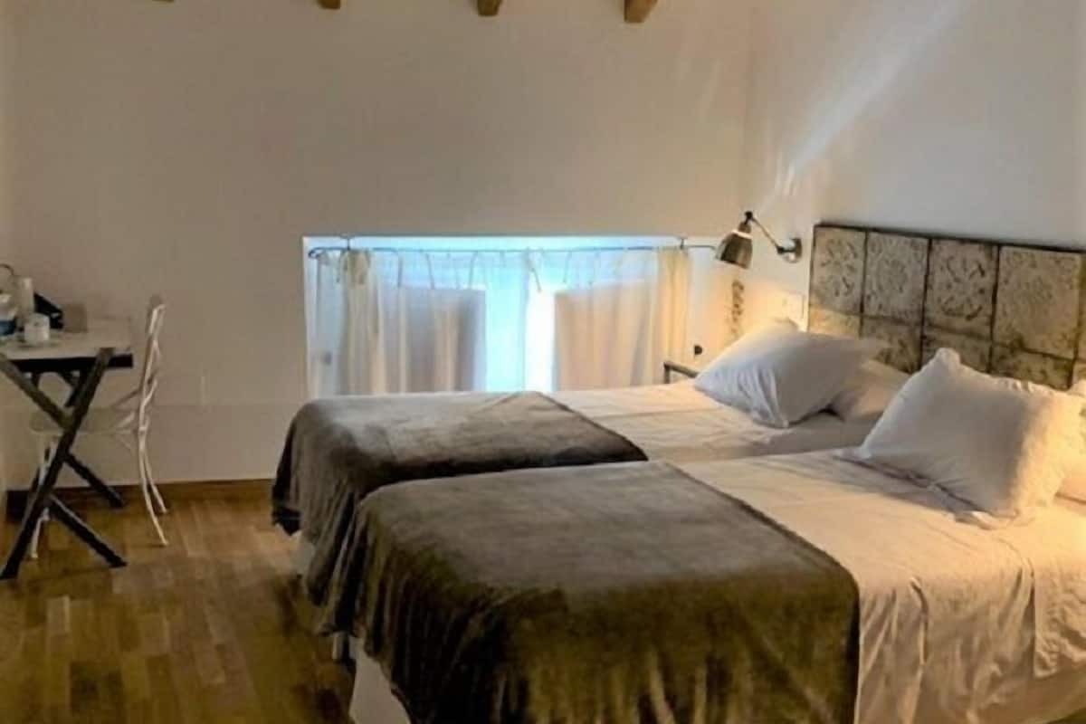 A bedroom with two beds, wooden beams on the ceiling, a desk, and a chair.