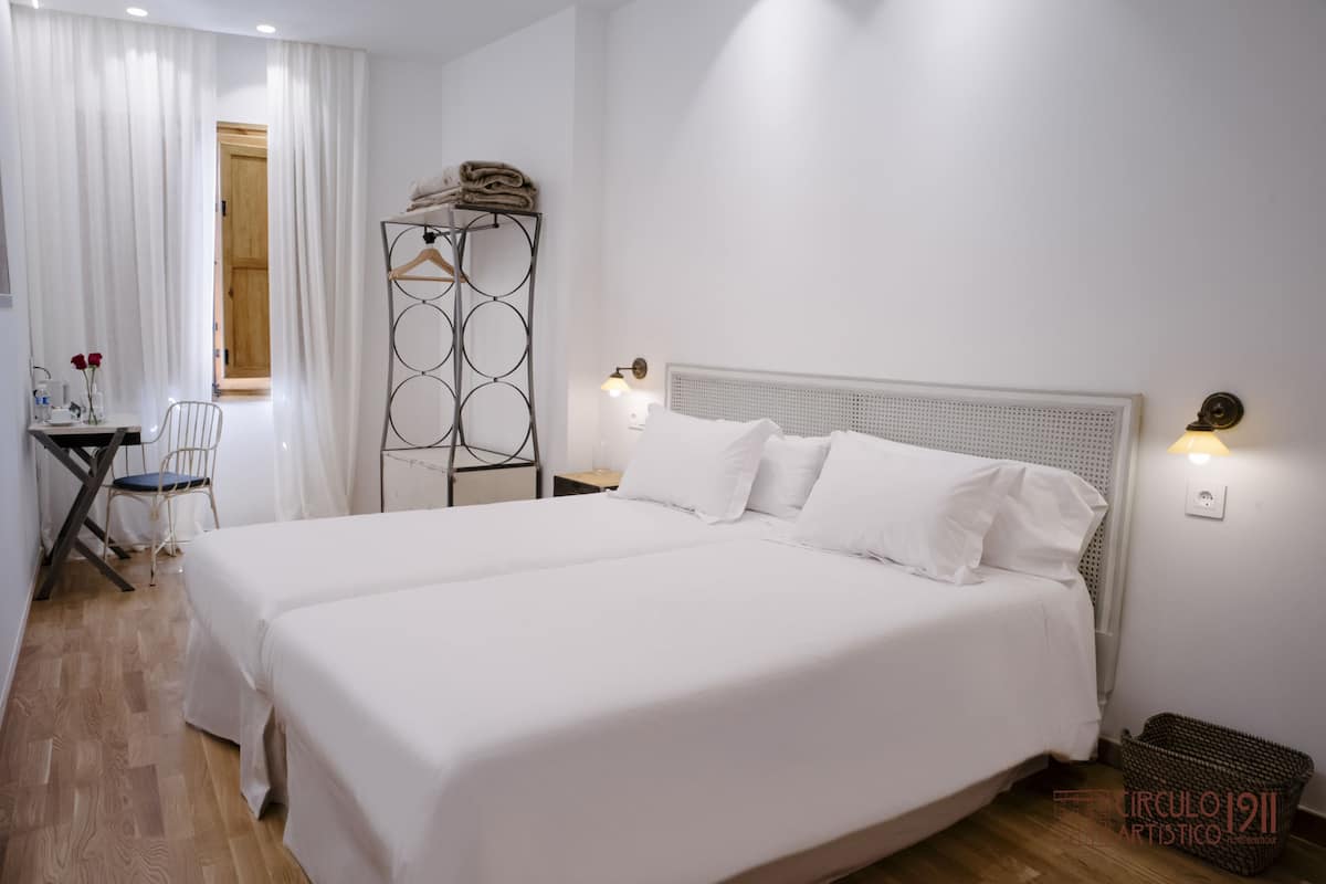 A hotel room with a large bed, a bedside table, a chair, and a wardrobe.