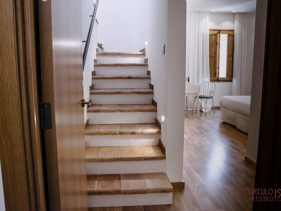 Una escalera de madera conduce a una habitación con una cama y una silla.