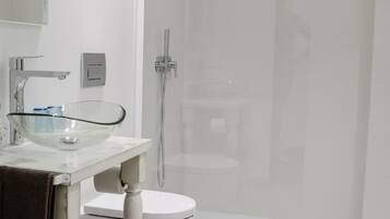 Een moderne badkamer met een glazen wastafel, een wit toilet en een inloopdouche.