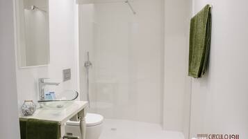 A modern bathroom with a glass sink, white toilet, and a walk-in shower.