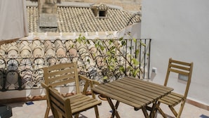Un balcon doté de mobilier en bois, une vue sur un bâtiment historique avec un clocher et un toit recouvert de tuiles.