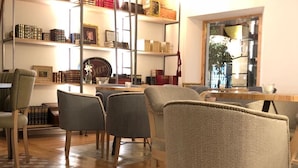 Un espace repas avec des tables et des chaises en bois, un tapis à motifs et des étagères remplies de livres et d’objets décoratifs.