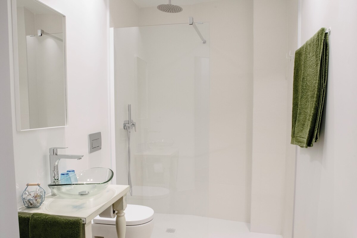 Un baño moderno con lavamanos de vidrio, inodoro blanco y ducha a pie.