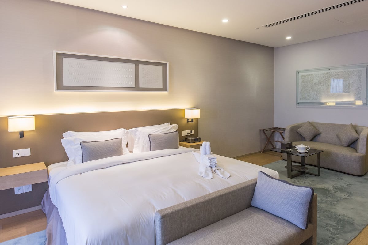 Une chambre d’hôtel avec un grand lit, des lampes de chevet, un canapé, une petite table et une œuvre d’art accrochée au mur.
