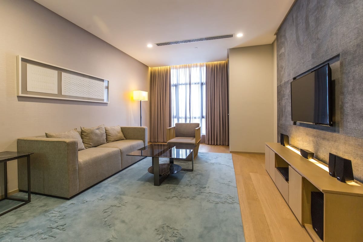 Un salon moderne comprenant un canapé, un fauteuil, une table basse, un téléviseur et une grande fenêtre avec des rideaux.