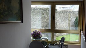 Ein Essbereich mit Tisch und Stühlen, einer Blumenvase und Blick auf eine Steinmauer und einen Garten durch ein Fenster.