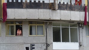 Ein zweistöckiges Gebäude mit einem Balkon, einem Fenster, durch das eine Person zu sehen ist, und einer Ampel.