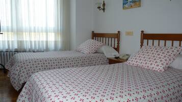 A room with two beds, each with a floral-patterned bedspread, a wooden headboard, and a bedside table with a lamp and a telephone.