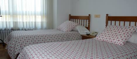 A room with two beds, each with a floral-patterned bedspread, a wooden headboard, and a bedside table with a lamp and a telephone.