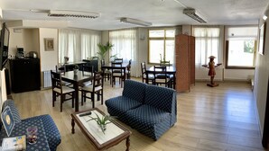 Ein Wohnzimmer mit Sofa, Couchtisch, Esstisch und Stühlen. Es gibt eine Küchenzeile mit Kühlschrank und Kaffeemaschine.