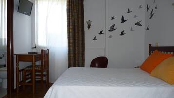 Un dormitorio con una cama, un escritorio, una silla, un televisor y una pared decorada con diseños de pájaros.