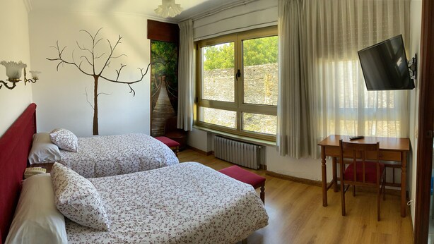 Ein Schlafzimmer mit zwei Betten, einem Fernseher, einem Fenster mit Blick und einem roten Kopfteil.