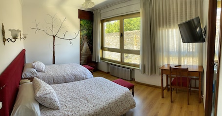 A bedroom with two beds, a TV, a window with a view, and a red headboard.