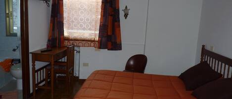 Un dormitorio con cama, escritorio, silla, televisor y ventana con cortinas.