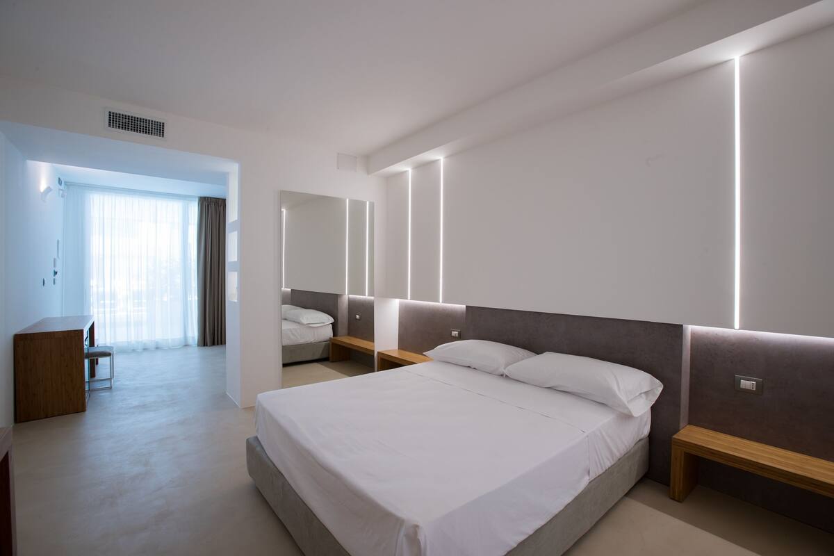 A modern bedroom with a large bed, bedside tables, a desk, and a mirror.