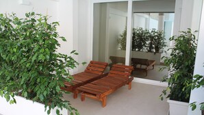 A balcony with wooden lounge chairs and potted plants.