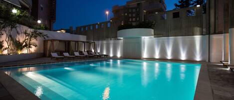 An indoor swimming pool with clear water, surrounded by lounge chairs and a low wall.
