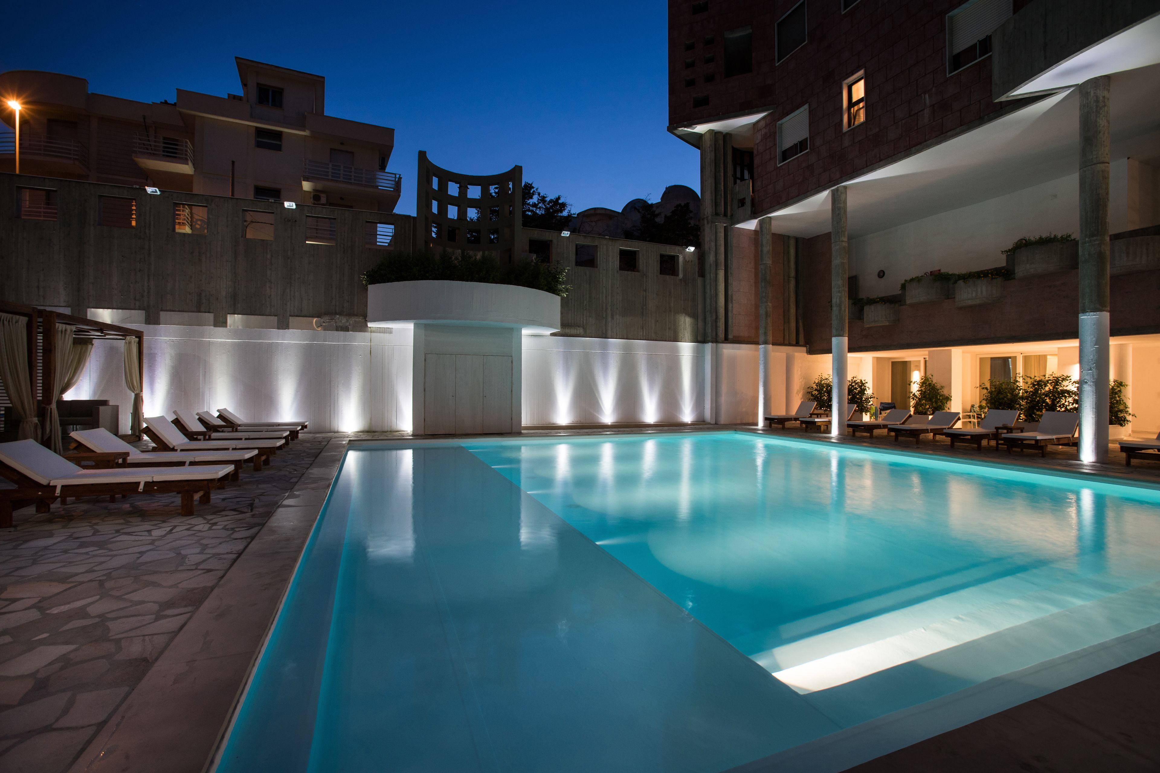 Piscina interna com espreguiçadeiras e piso de pedra, cercada por edifícios com varandas e janelas.