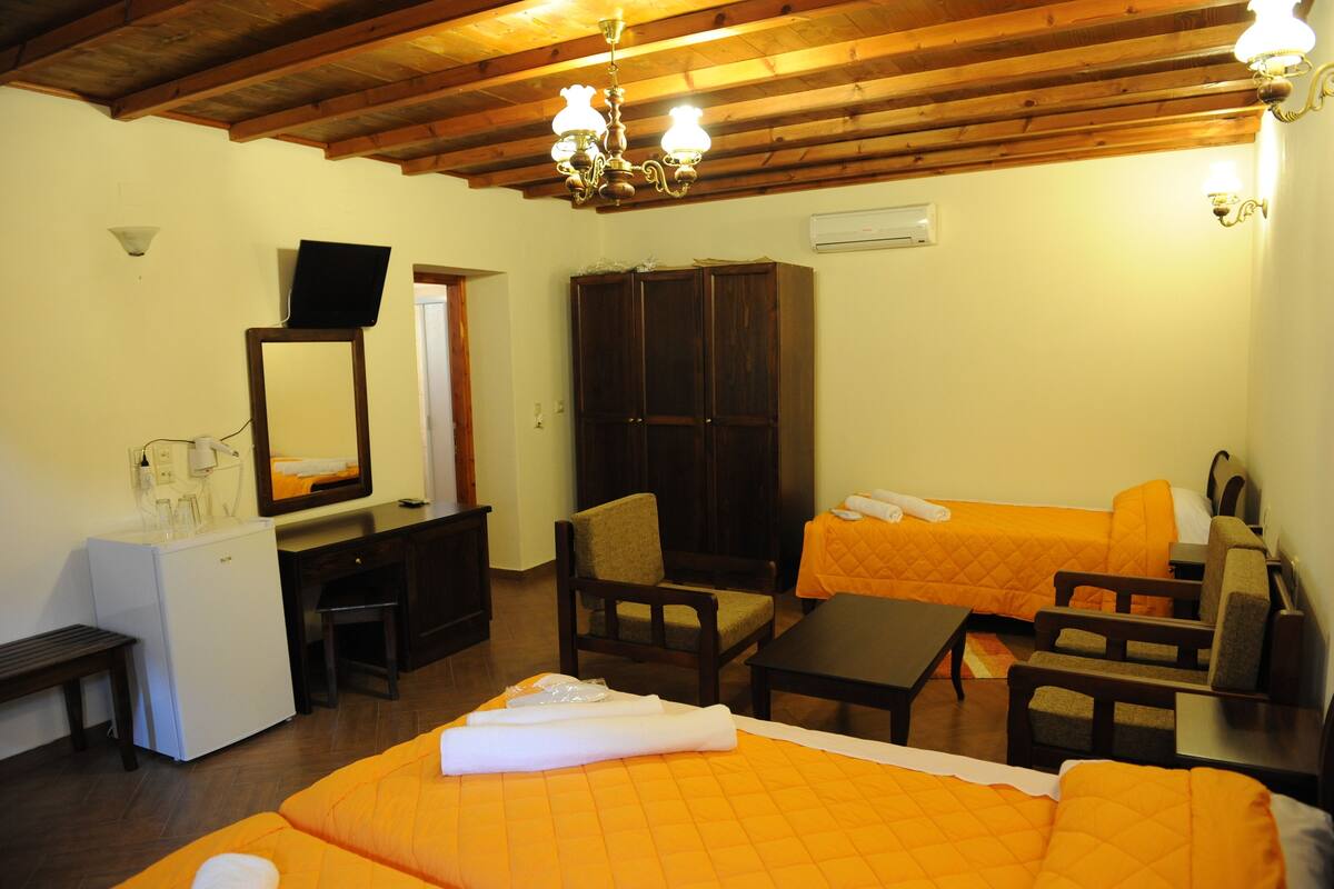 Une chambre d’hôtel comprenant un lit, deux chaises, une petite table, un bureau avec un miroir, une armoire et un luminaire au plafond.
