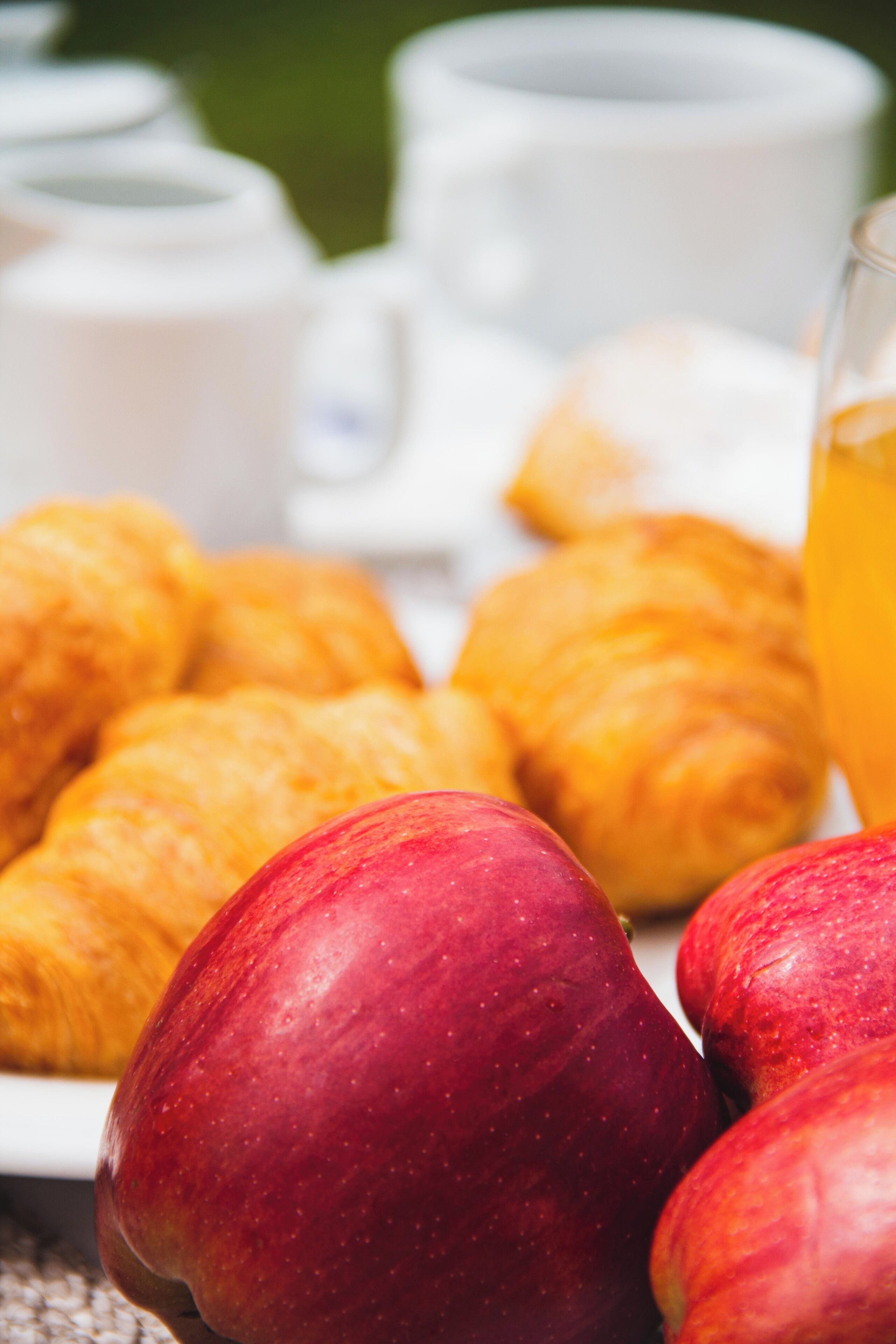 A breakfast setting with croissants, apples, and a glass of orange juice.