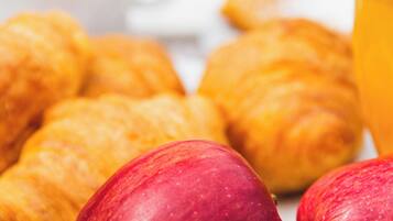 A breakfast setting with croissants, apples, and a glass of orange juice.