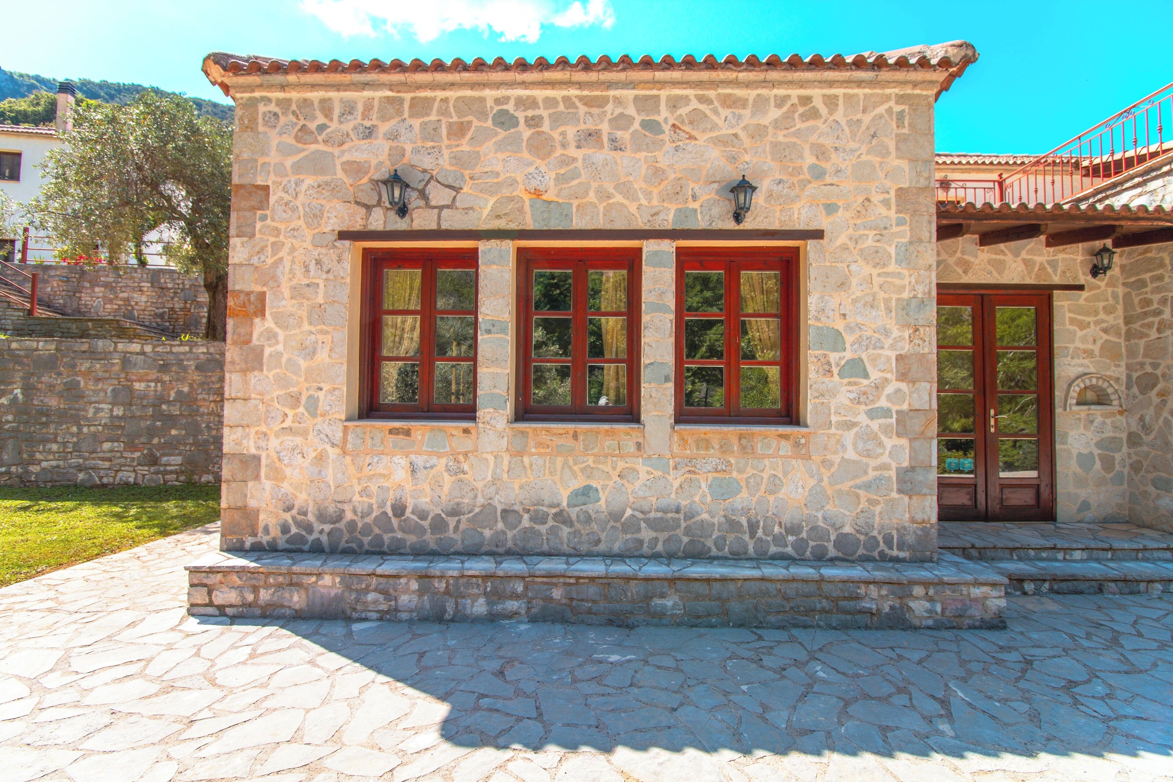 A stone building with a tiled roof, a set of steps leading to the entrance, and a small balcony with a red railing.