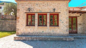 A stone building with a tiled roof, a set of steps leading to the entrance, and a small balcony with a red railing.