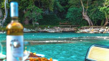 A table with a bottle and food, overlooking a river with rocks and trees in the background.