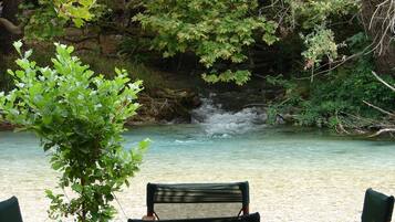 Vista de un río con cascada, rodeado de follaje y árboles. Hay dos sillas mirando al río.