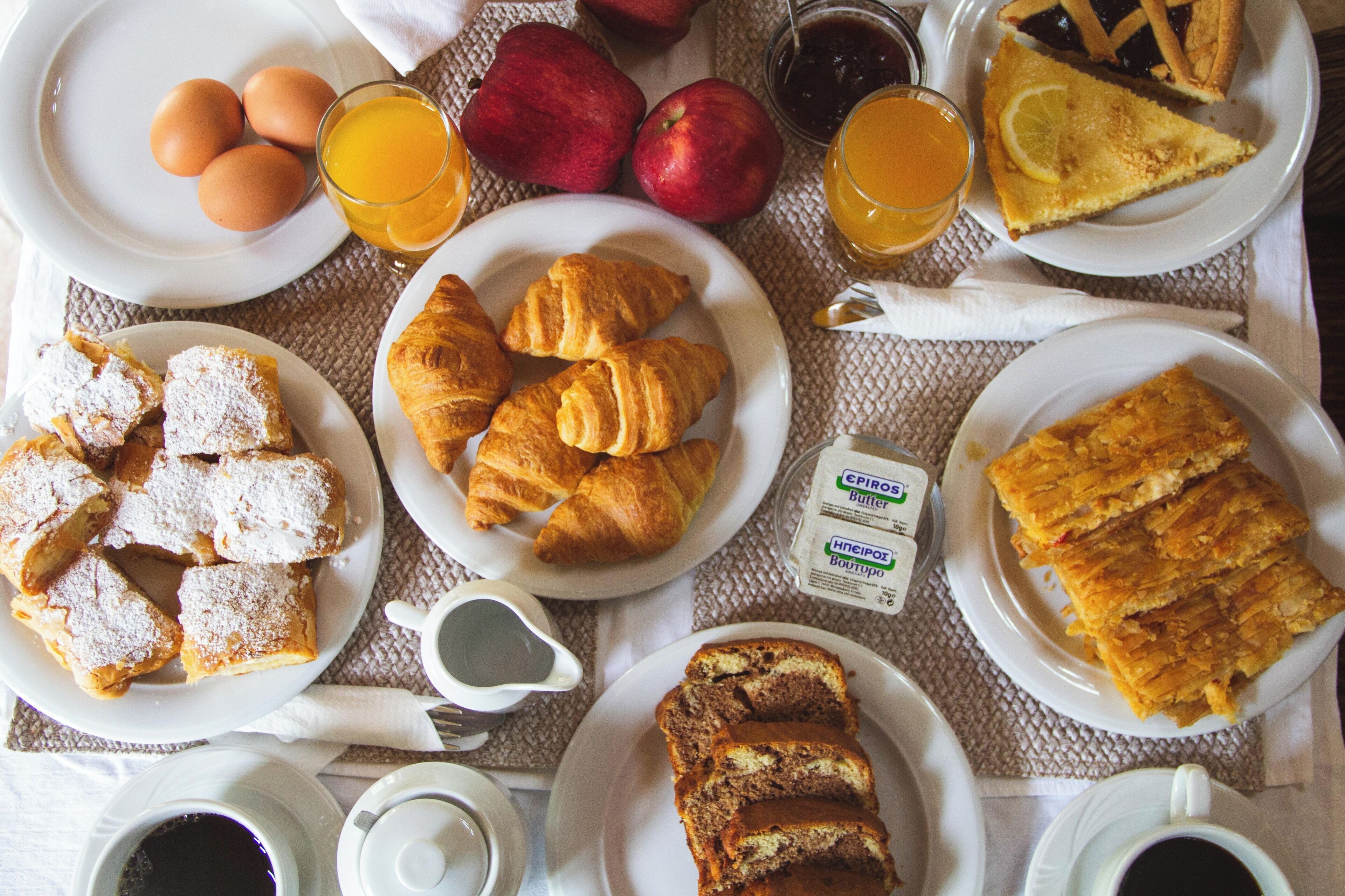 A breakfast table with plates of eggs, croissants, and pastries, along with fruits and beverages.