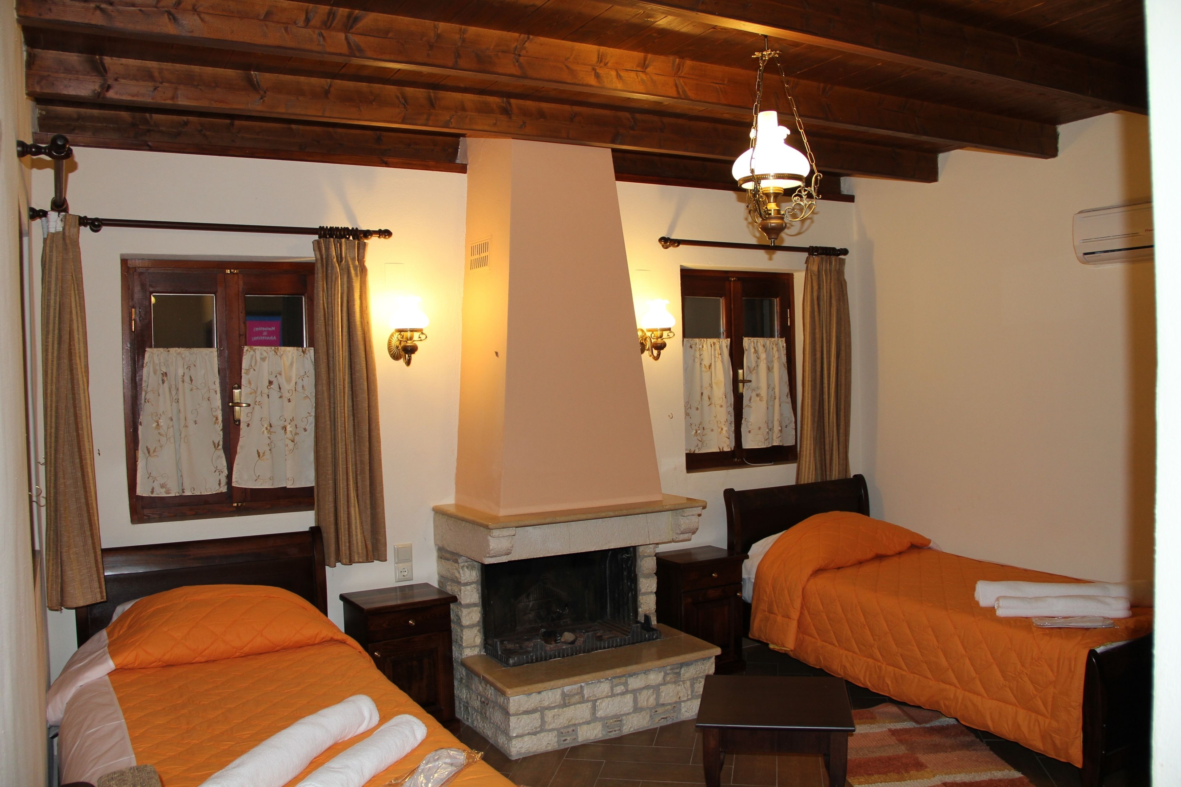 Une chambre avec deux lits, une cheminée en pierre, des poutres apparentes et des appliques murales.