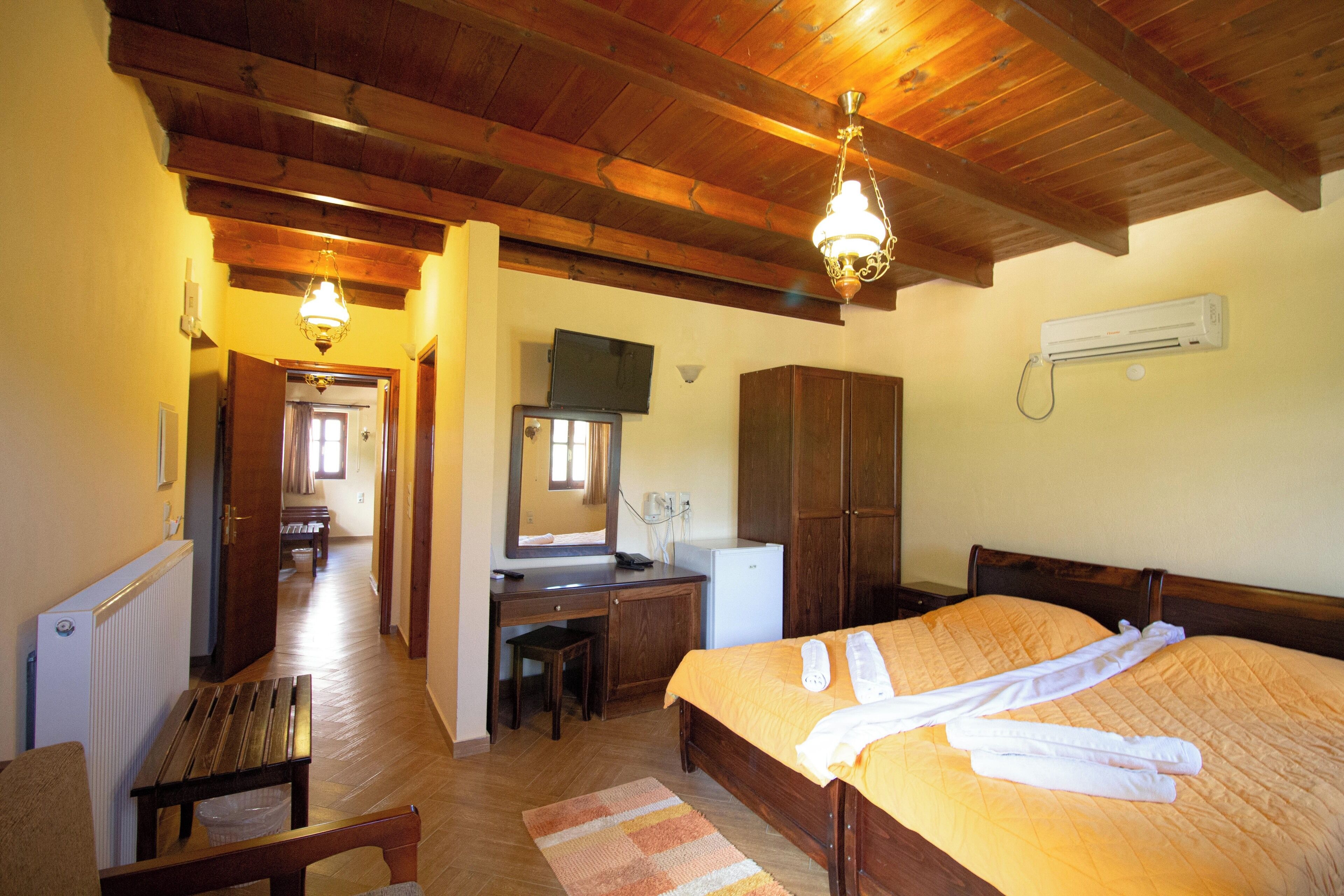 A hotel room with a wooden ceiling, a bed with white towels, a desk, a chair, a radiator, and a television.