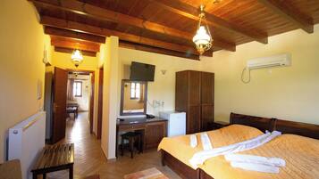 A hotel room with a wooden ceiling, a bed with white towels, a desk, a chair, a radiator, and a television.