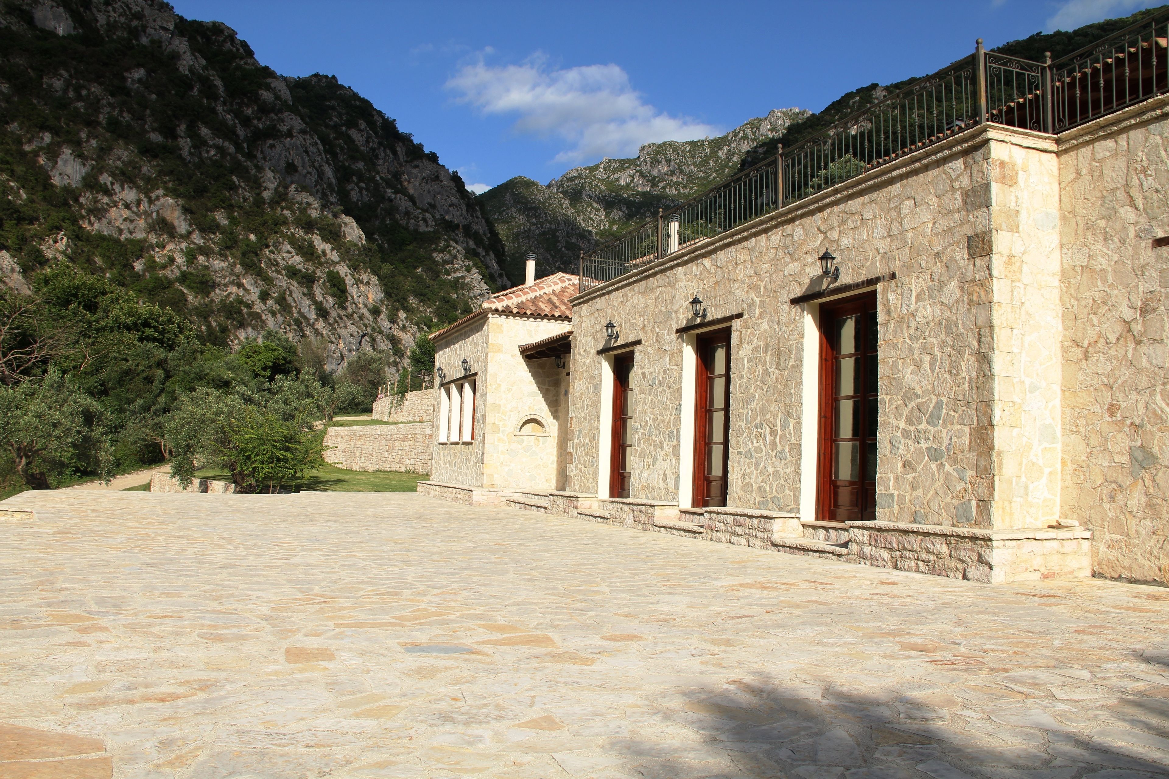 Un edificio de piedra con patio, telón de fondo de montaña y baranda metálica en el piso superior.