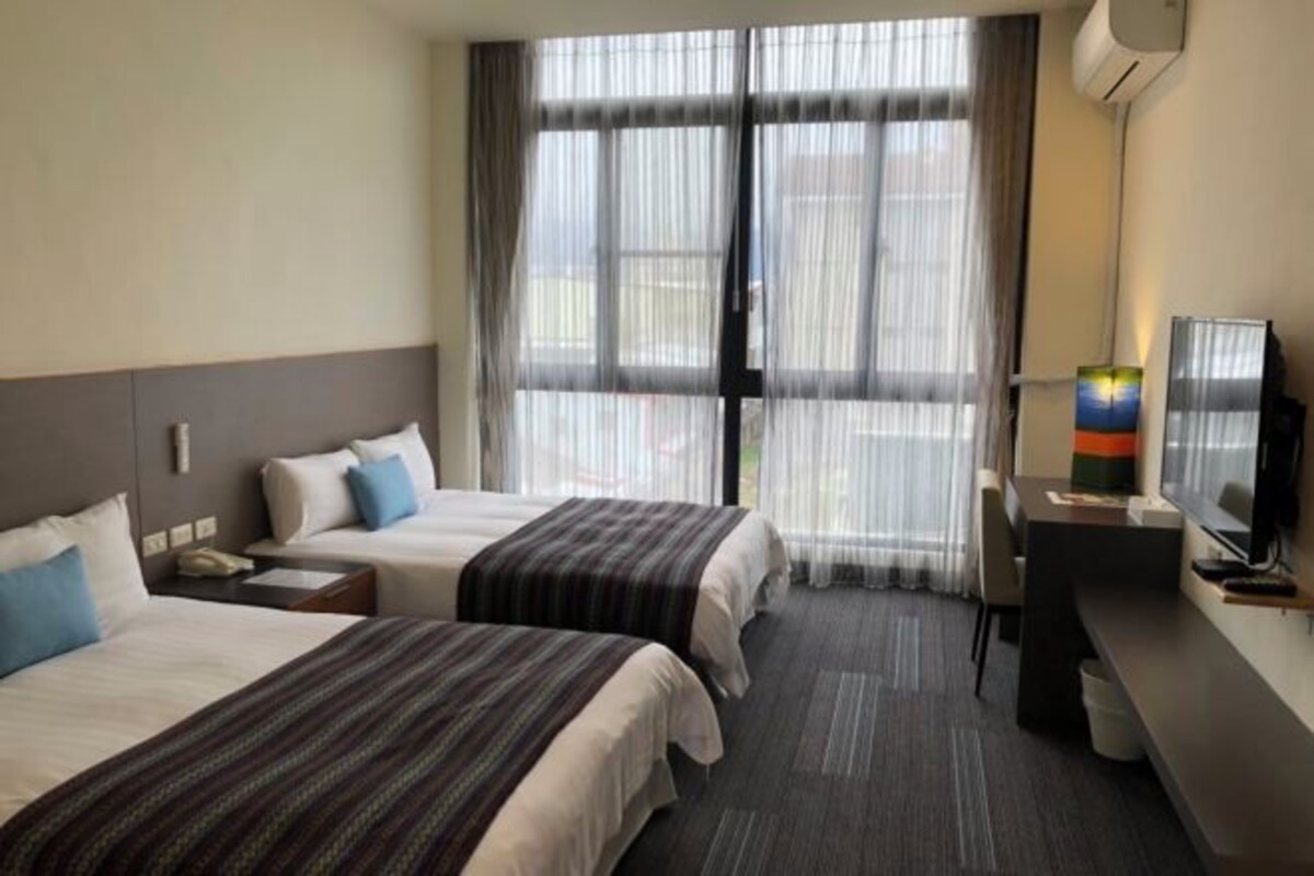 A hotel room with two beds, a desk, a chair, and a television.