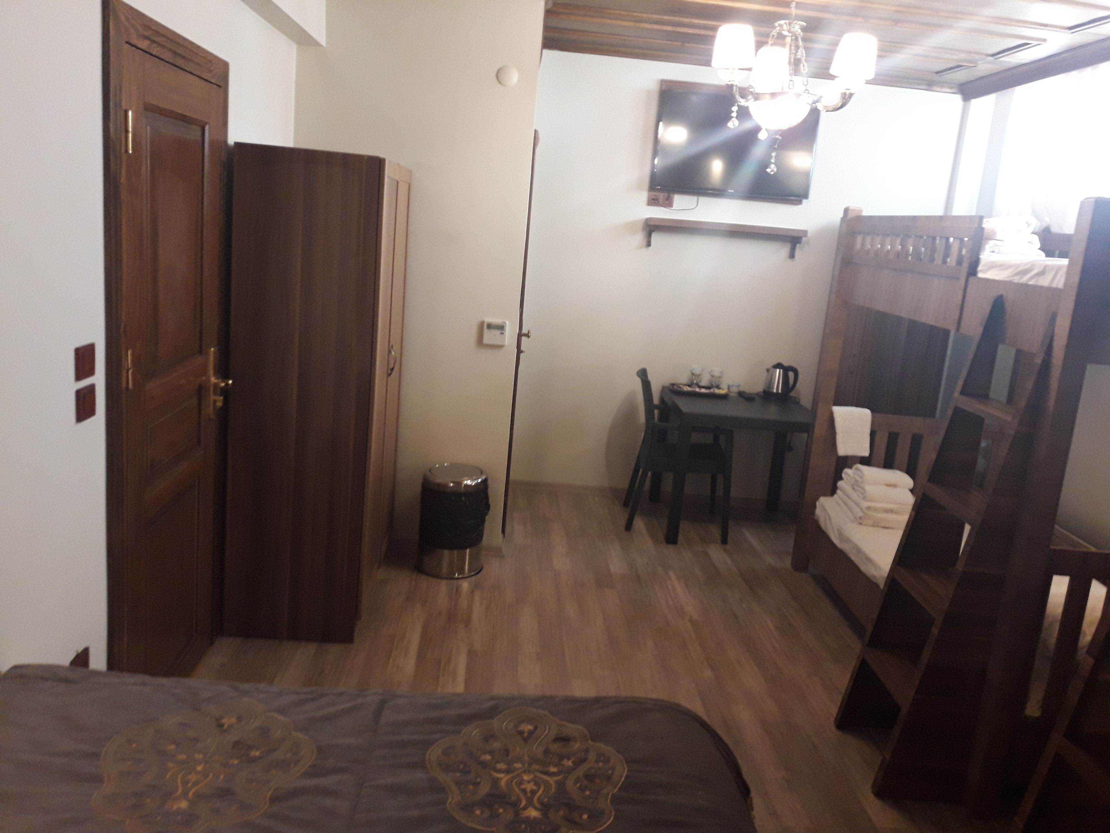 Quarto com cama, escrivaninha, cadeira, TV fixada na parede e guarda-roupa de madeira.