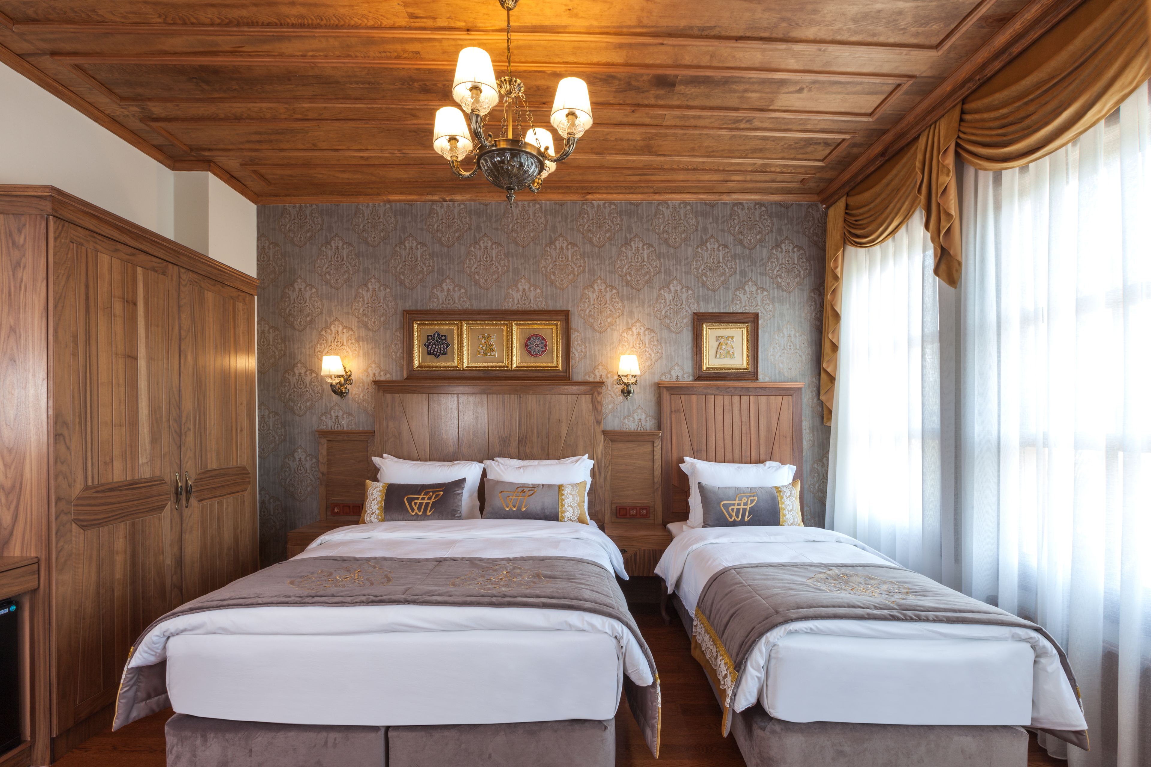 A hotel room with two beds, wooden headboards, a chandelier, and framed pictures on the wall.
