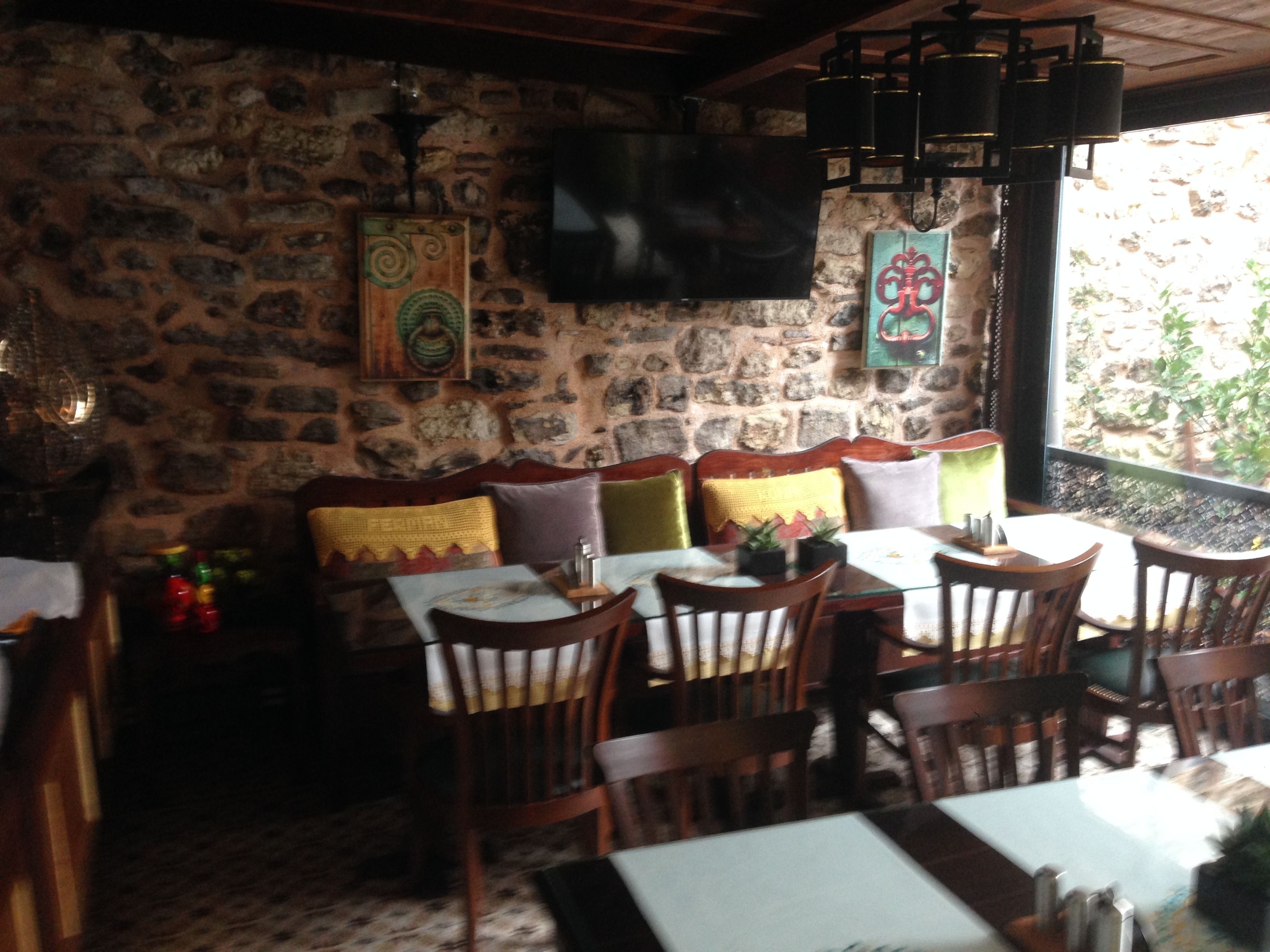 Un restaurant aux murs de pierre, doté de meubles en bois et d’un téléviseur à écran plat fixé au mur.