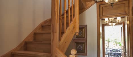 A wooden staircase with a handrail, leading to a tiled hallway with a chandelier.