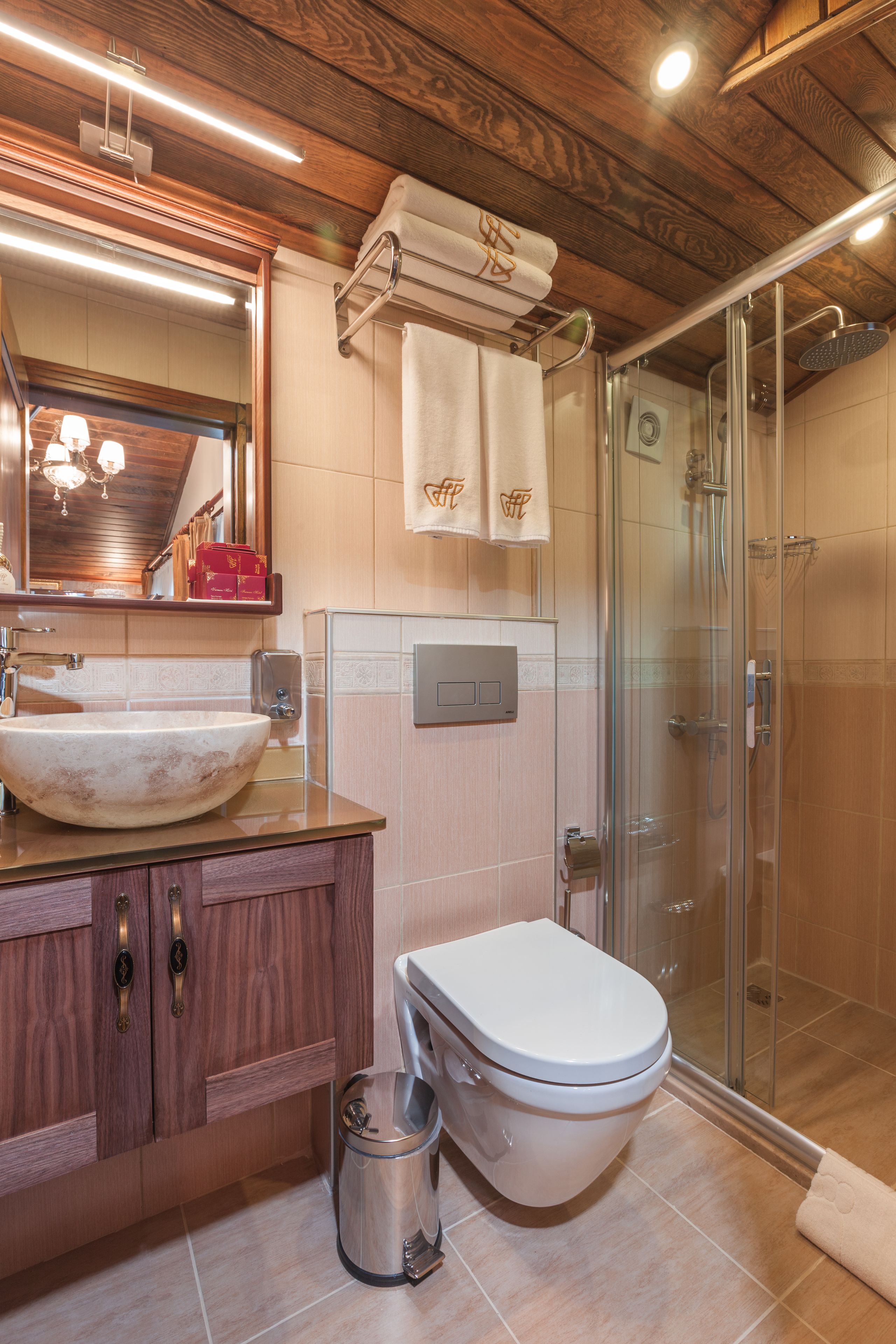A bathroom with a wooden ceiling, a large mirror, a sink, a toilet, and a glass-enclosed shower.
