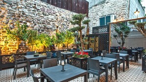 Un área de comedor al aire libre con muros de piedra, mesas y sillas.