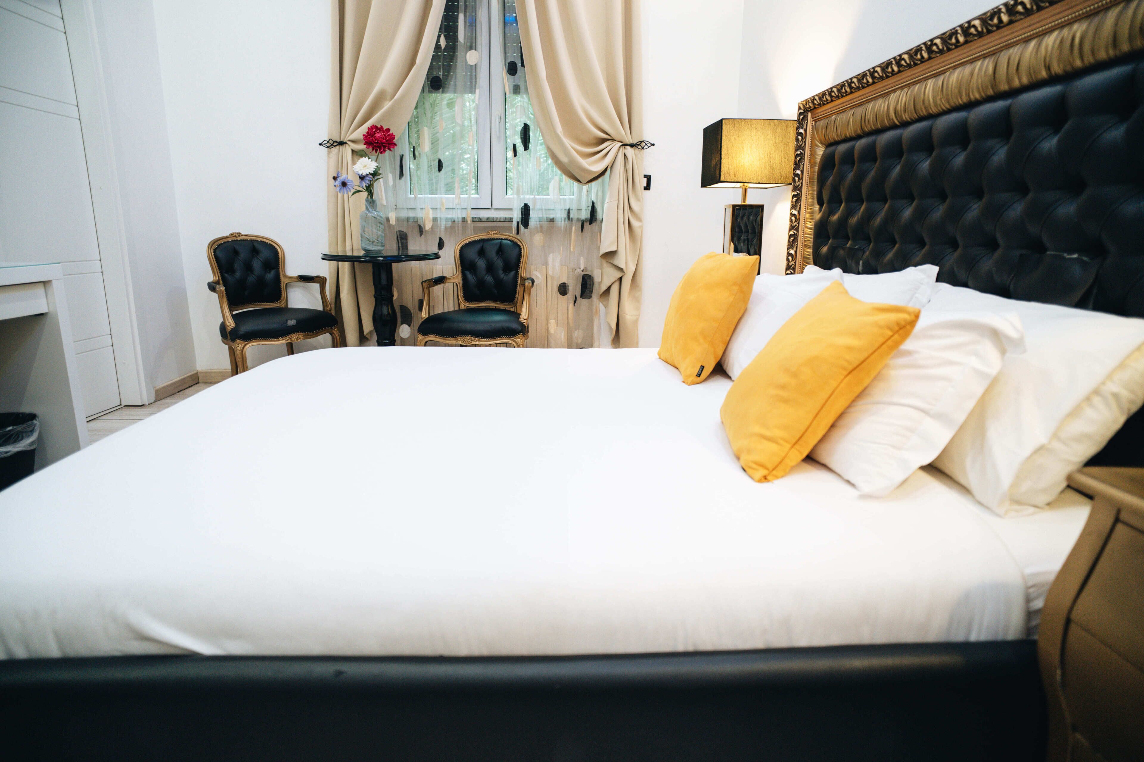 A large bed with white linens and two yellow pillows, a black upholstered headboard, and a small table with a lamp beside it.
