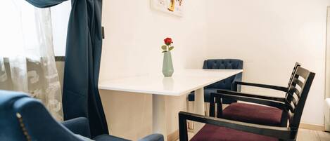 A dining area with a white table, blue chairs, a vase with a red flower, and a painting on the wall.