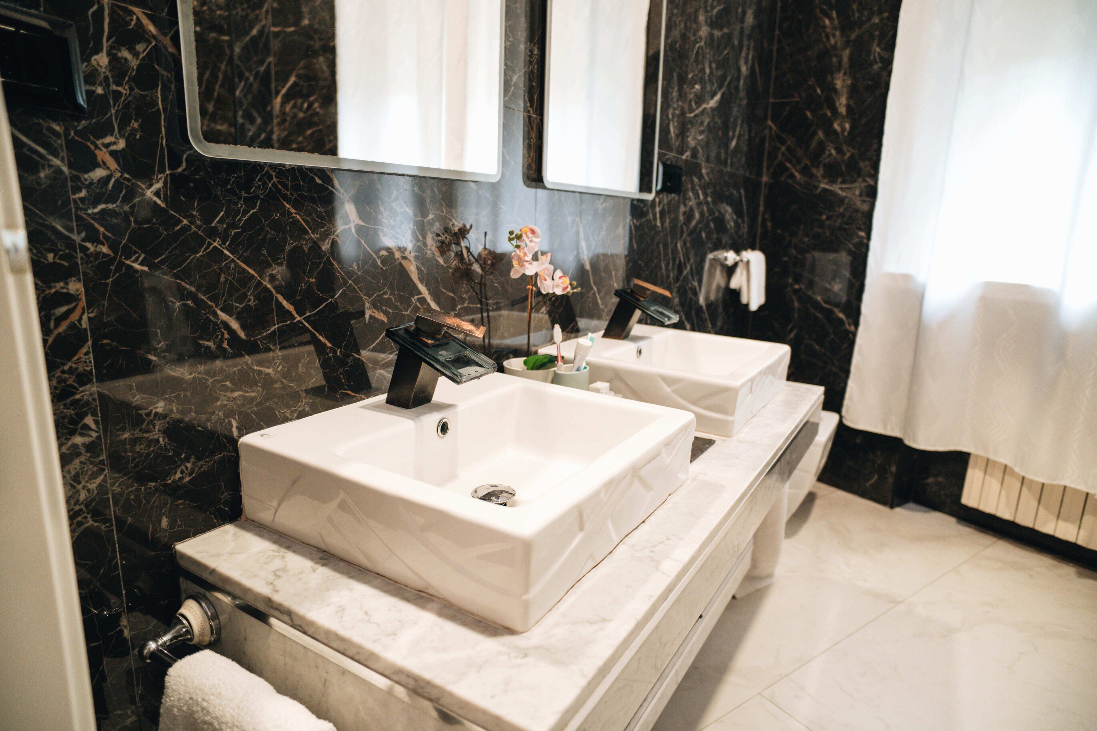 A bathroom with two sinks, marble walls, and a large mirror.