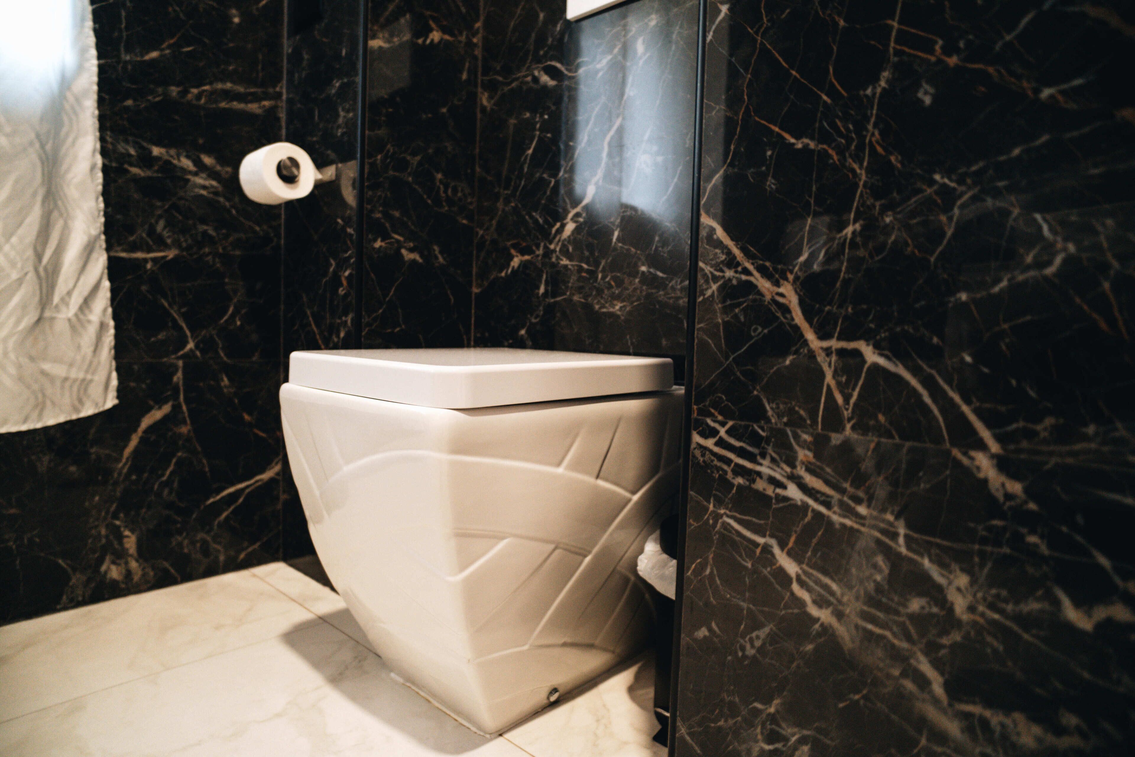 Ein modernes Badezimmer mit Toilette, Marmorwänden und einem weißen Handtuch an der Wand.