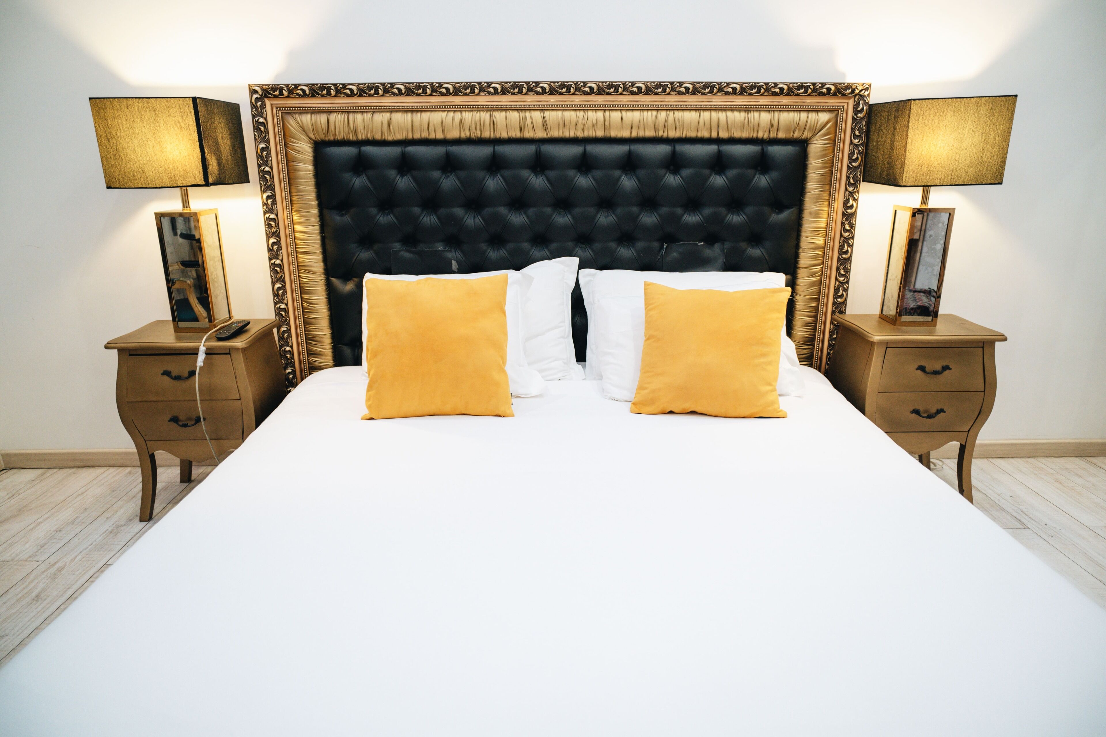 Una cama bien hecha con cabecera capitonada, dos mesitas de noche con lámparas y suelo de madera.